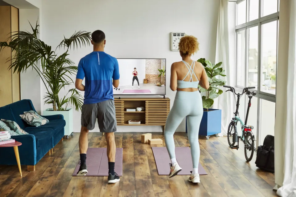 Rear view of couple watching online exercise class on TV and working out in living room. 